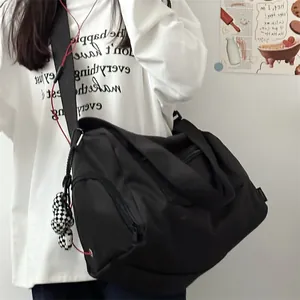 Detailed view of large black sports duffel bag with checkerboard charm on model