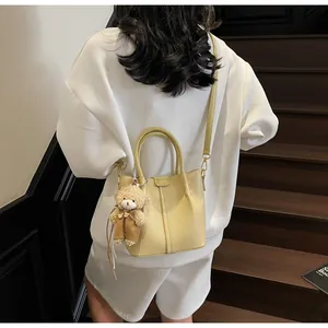 Detail of beige textured leather tote bag with cute teddy bear charm on model