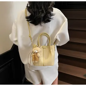 Detail shot of pale yellow crossbody bag with cute teddy bear charm on model
