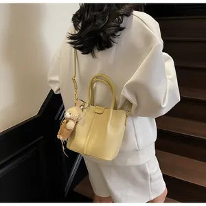 Detail of cream bucket bag with litchi texture and a cute plush bear charm decoration