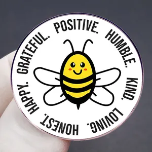 Épinglette abeille avec des mots positifs comme KIND et HAPPY sur fond blanc