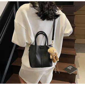Detail of black pebbled leather bucket bag with top handles and cute bear charm accent