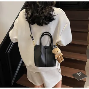 Detail of black lychee grain leather bucket bag with cute bear charm on a staircase
