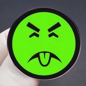 Cartoon sad face metal alloy pin badge in fluorescent green held by a hand