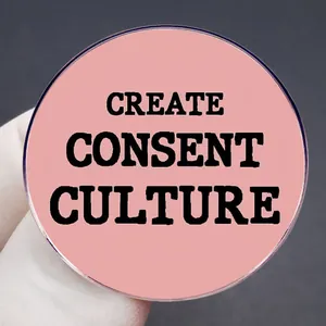 Pink Create Consent Culture enamel pin held against a professional dark background