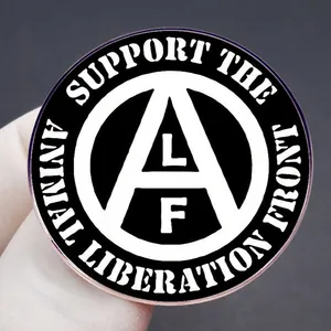Black and white Animal Liberation Front badge held by a gloved hand on dark background