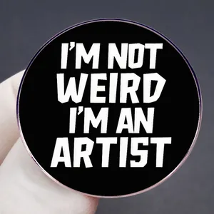 Black round enamel pin badge with 'I'M NOT WEIRD I'M AN ARTIST' bold text design