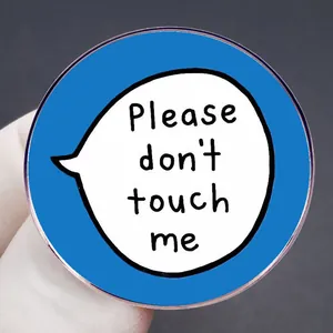 Pin redondo azul con bocadillo de texto Please don't touch me sujetado en la mano aquí