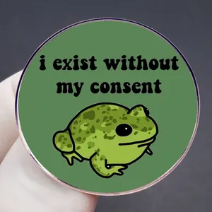 Funny green frog badge with 'i exist without my consent' text in hand shot