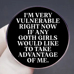 Round black gothic brooch with white text slogan shown in a close-up finger grip