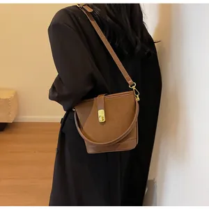 Detail view of brown frosted bucket bag featuring a gold square twist lock and smooth leather