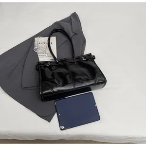 Flat lay of a black glossy shoulder bag with silver buckles and lifestyle accessories