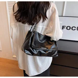Detail view of black glossy leather tote bag with silver chain strap on model's shoulder