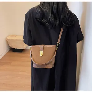 Detail of a caramel brown frosted bucket bag with gold metal clasp on a black coat