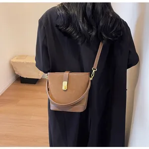Detail of a dark brown suede bucket bag featuring a gold buckle and elegant shoulder strap