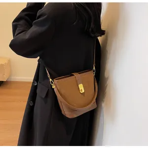 Close-up of matte brown bucket bag featuring gold metal buckle and suede patchwork detail