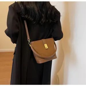Brown frosted suede bucket bag with leather strap worn over a black winter coat