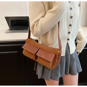 Detail of caramel suede baguette bag with dual front pockets worn on the shoulder