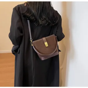 Detail of dark brown matte bucket bag with golden metal lock on a black wool coat