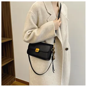 Sac bandoulière noir en cuir avec boucle dorée porté par un mannequin en manteau