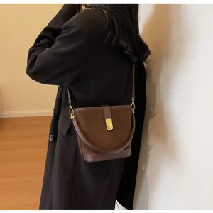 Detail of dark brown suede bucket bag featuring smooth leather trim and golden metal clasp