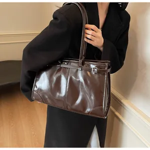 Detail of a large dark brown patent leather tote bag with silver buckle worn by a model