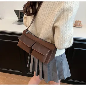 Detail of retro brown suede baguette bag featuring dual utility pockets and metal zipper