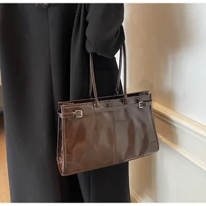 Deep brown glossy leather tote bag shown on a model in a minimalist indoor setting