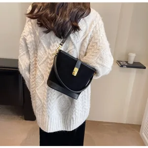 Detail of black suede bucket bag with gold hardware worn on white knitted sweater