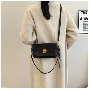 Détail d'un sac bandoulière en cuir noir avec boucle dorée et foulard en soie décoratif