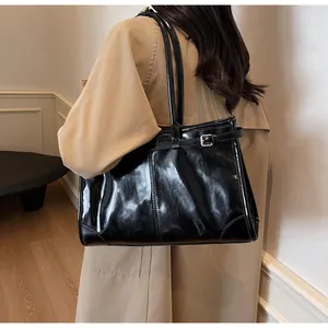 Close-up of a glossy black leather tote bag with stylish side buckle detail on model