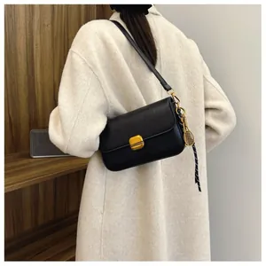 Détail du sac bandoulière en cuir noir avec boucle dorée et pendentif de raquette de tennis