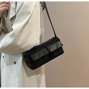 Detailed view of a black faux suede baguette bag with symmetrical front flap pockets