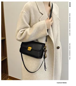 Détail du sac bandoulière en cuir noir mat avec boucle dorée et pendentif tissé élégant