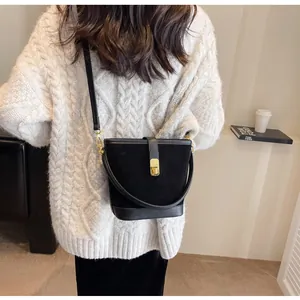 Model wearing a black matte suede bucket bag with leather straps and metal lock closure