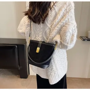 Detailed close-up of a black bucket bag with gold hardware worn over a white sweater