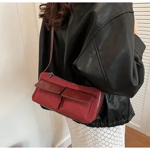 Detail of burgundy baguette bag with dual front pockets worn over a black leather jacket
