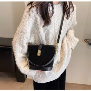 Detail of black matte suede bucket bag with gold buckle and leather trim on a model