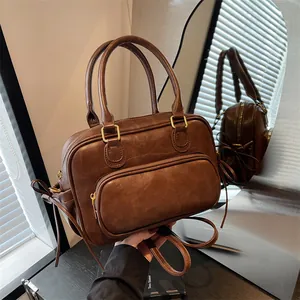 Vintage brown leather Boston bag with dual handles and front pocket on reflective surface