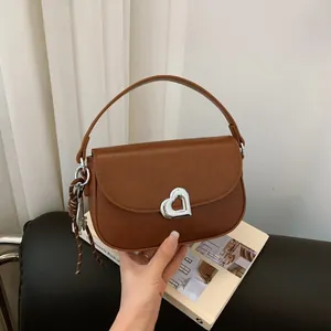 Brown leather shoulder bag with a silver heart buckle and decorative woven strap