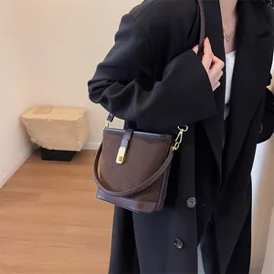 Deep brown matte suede bucket bag with gold buckle on a stylish model in a black coat