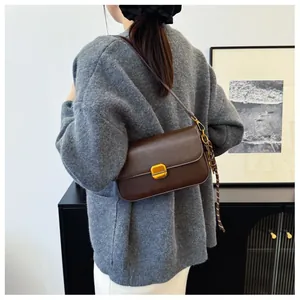 Détail du sac bandoulière en cuir marron foncé avec boucle dorée et foulard en soie décoratif