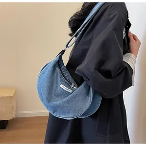 Detail of blue denim crescent bag with fashion label and silver metallic zipper closure