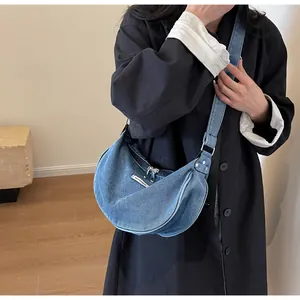 Detail of light blue denim crescent bag with white fashion tag and silver metal zipper