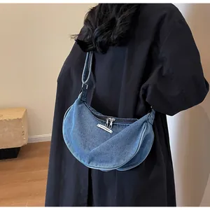 Detail of blue denim crescent bag featuring a fashion woven label and dual zippers