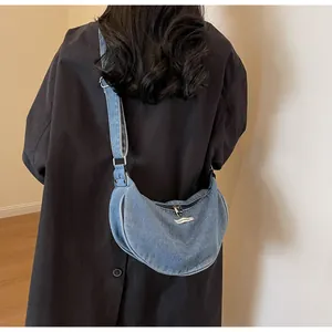 Detail of light blue washed denim crescent bag with adjustable strap and zipper