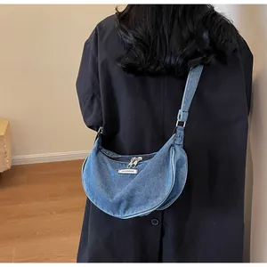 Detail of blue denim crescent bag with Fashion & Bag label and dual zipper closure