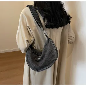Side view of a dark grey washed denim crescent bag worn over a beige trench coat