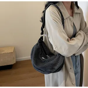 Detail of dark gray washed denim crescent bag with fashion tag and adjustable strap