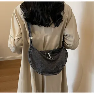 Detail of dark denim crescent bag worn over a trench coat for a casual commuting look